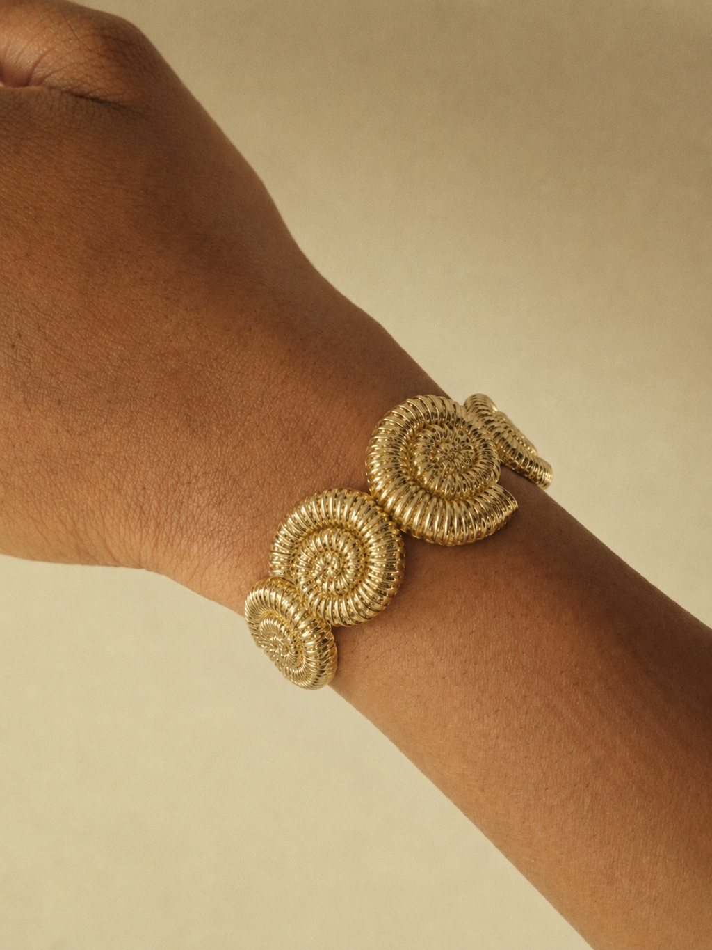 Gold bracelet on a wrist with a plain background