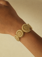 Gold bracelet on a wrist with a plain background